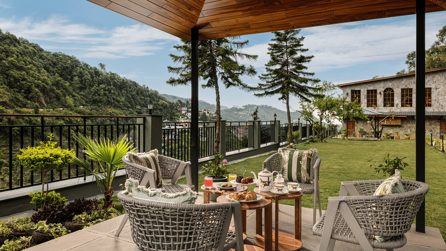 Covered outdoor patio dining area overlooking a green mountain valley with clear blue skies.