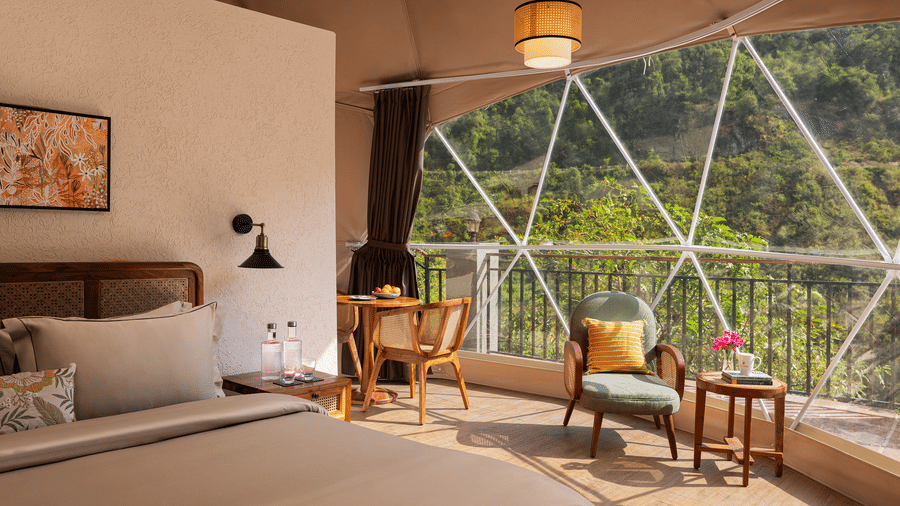Cozy bedroom setup inside a geodesic dome structure with a large window displaying a lush mountain view.