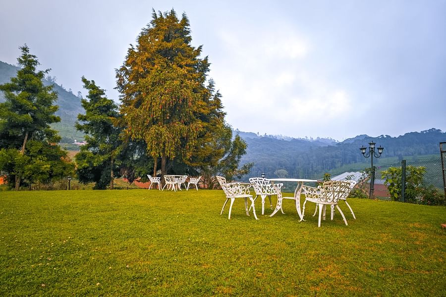 Metal seats and table kept on a lawn area with trees next to it - Ibex Stays & Trails, Coonoor (Leewood).