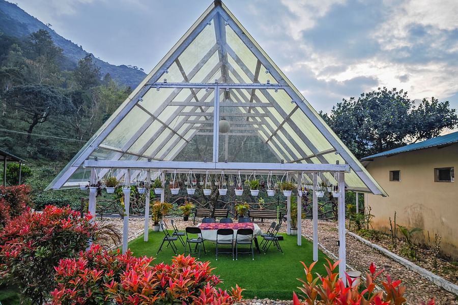 An outdoor space with a glass roof, comfortable seating underneath and a forest in the background making it one of the best couple friendly hotels in valparai - Ibex Stays & Trails, Valparai (Mistly)