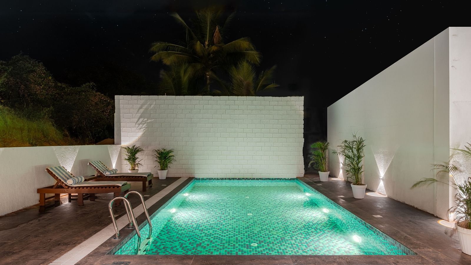 Outdoor pool area with green lighting and privacy walls at night at Bedzzz Xclusiv Morjim, Goa