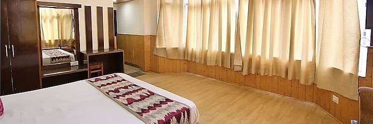 A view of a room at DLS Hotel Devlok, Manali with a double bed and windows covering the wall in front of the bed