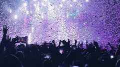 Concert crowd enjoying a show with purple confetti falling from above.