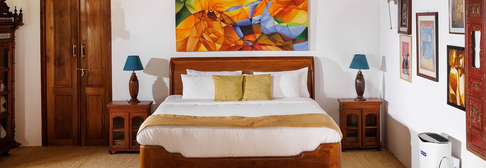 A room with wooden interiors featuring a bed, bedside tables, and paintings hung on the wall - BluSalzz Villas - Muhamma Resort, Alleppey