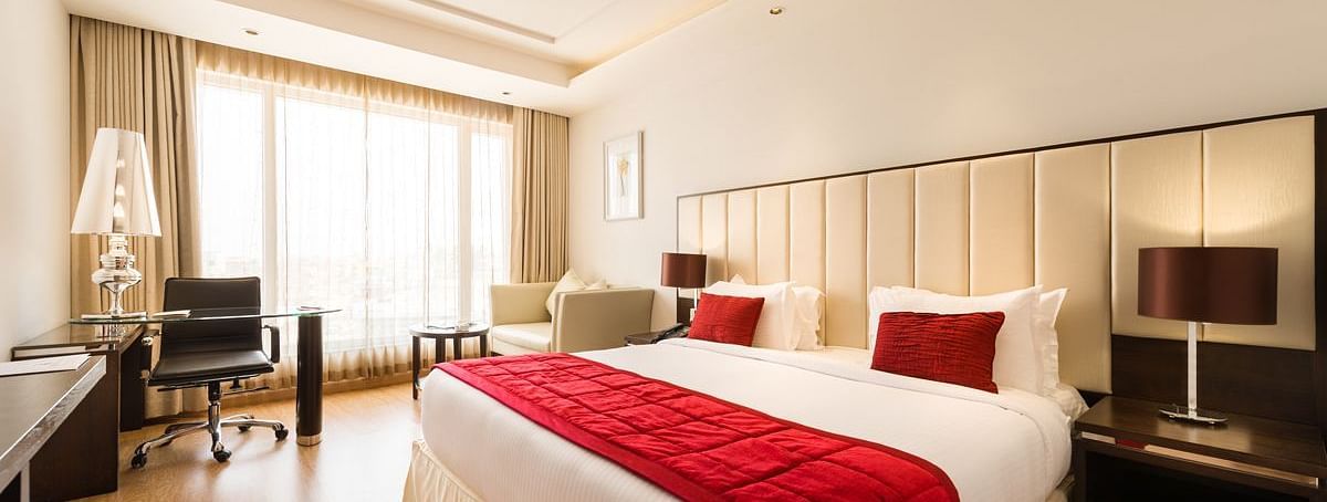 A well-lit hotel room with two twin beds covered in red bedspreads and white sheets - TGI Grand Fortuna, Hosur