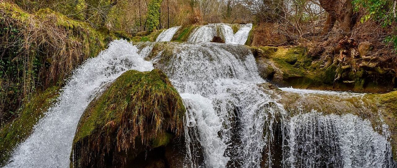 a stream of water cascading through huge rocks in the middle of a forest