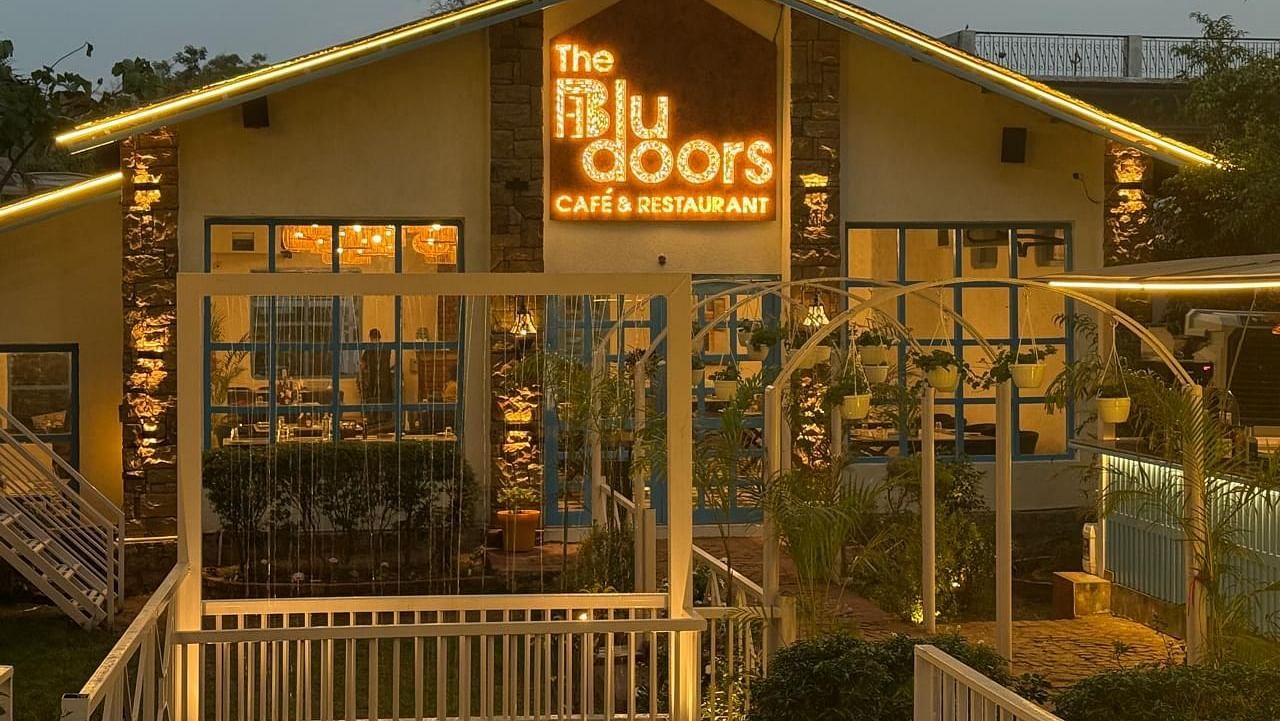 The Blu Doors Cafe and Restaurant' exterior at dusk, with illuminated sign and warm glowing lights.