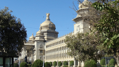 A grand, multi-storey stone building featuring ornate domes and columns, surrounded by manicured trees.