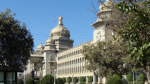 A grand, multi-storey stone building featuring ornate domes and columns, surrounded by manicured trees.