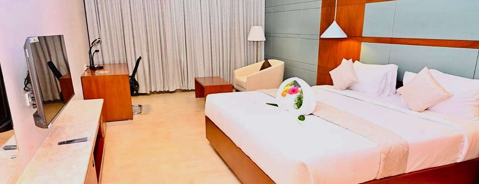 A Executive Suite at Dhanalakshmi Srinivasan Hotels, Perambalur featuring a neatly made bed with white linens and pillows, a wooden headboard, and a desk with a chair.