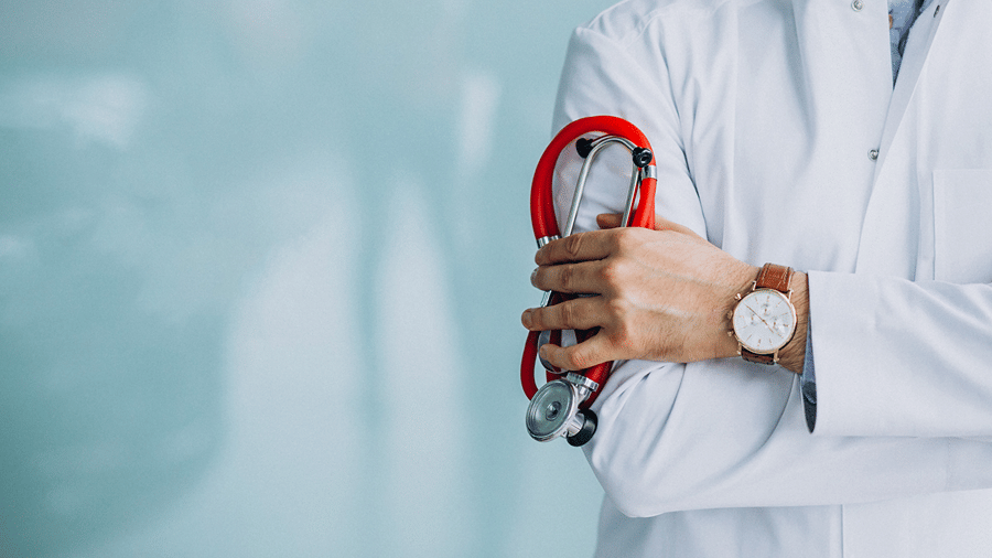 Close-up of a healthcare professional in a white medical coat holding a red stethoscope against a soft blue background.