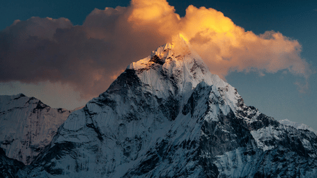 Sunset painting clouds golden over the rugged, snow-capped peak of Mount Everest in the Himalayan range of Nepal.