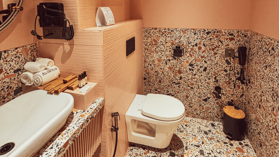 A bathroom featuring a white toilet, a washbasin on a speckled counter, and rolled towels on a rack at Avanya Resorts N Retreat.