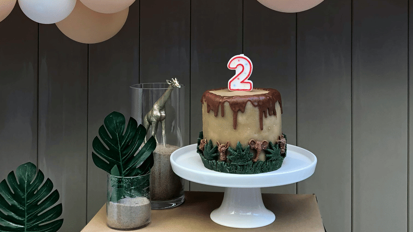 Decoration setup featuring a large arch of peach, gold, and pink balloons and a simple round cake.