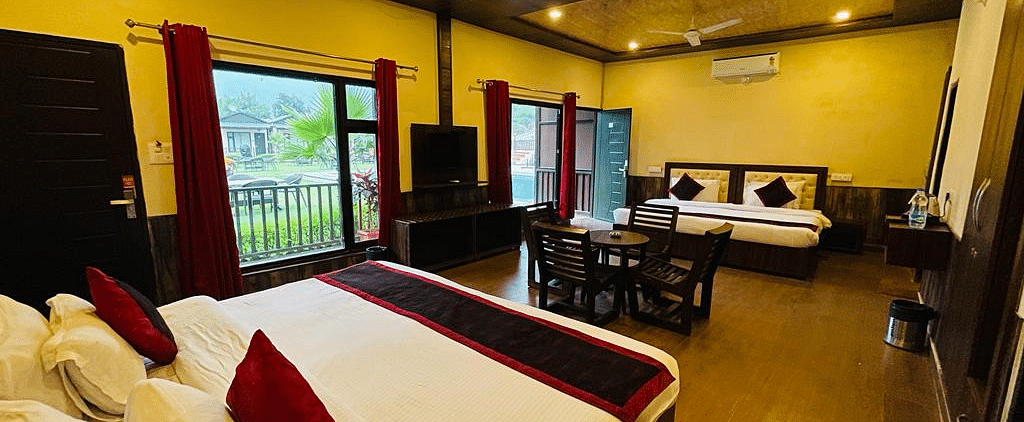 A Family Cottage with beds facing towards each other seperated by a round dining table and TV at DLS MJ River Resort, Rishikesh.