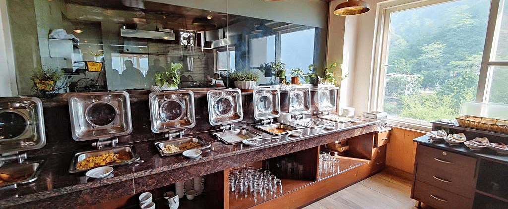 The buffet counter in the restaurant at Regenta Inn DLS overlooking the lush green views from the windows in the side.