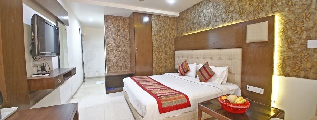 A hotel room with a textured accent wall, a plush bed with decorative pillows, a wooden table, and a TV, illuminated by warm ceiling lights. - Hotel Diamond Plaza, Chandigarh.