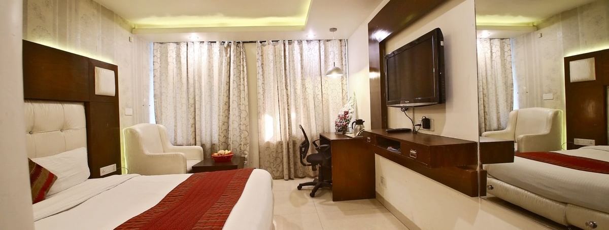 A hotel room with a plush bed, a red runner, a sofa, a TV, and a mirror. - Hotel Diamond Plaza, Chandigarh.