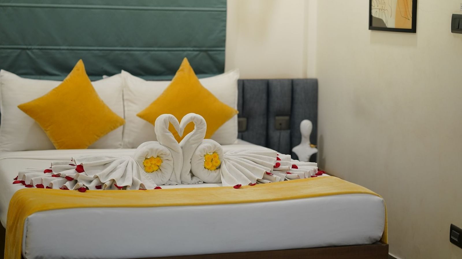 A room with a neatly made double bed adorned with yellow and towels shaped into swans, scattered with rose petals for a welcoming touch at Hotel Kyzen Smartstays – Smart, Reliable, Kyzen