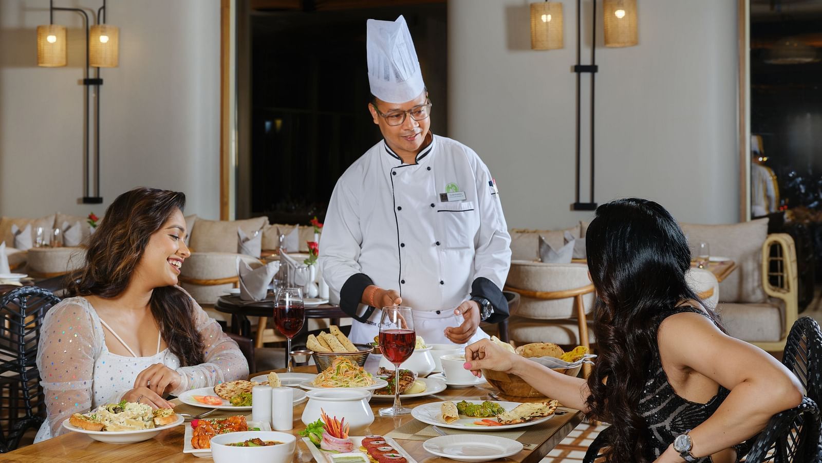 A chef elegantly serving to two women enjoying a gourmet meal in a beautifully lit restaurant with sophisticated interiors