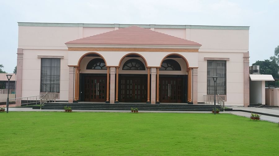 The exterior of a light-coloured building with an arched entrance and a green lawn in front - Kankidham Lords Inn