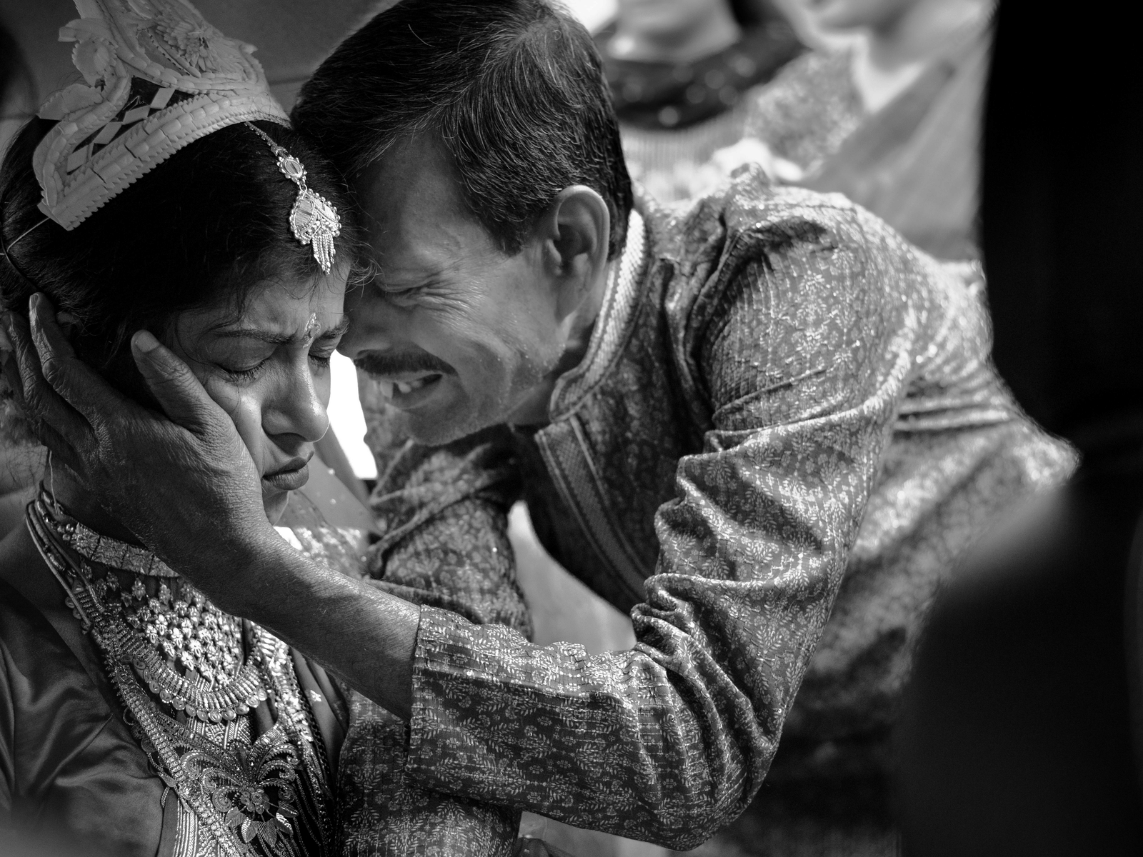 A heartfelt moment between a bride and an elder during a wedding ceremony, as he gently holds her face in an emotional and affectionate gesture.