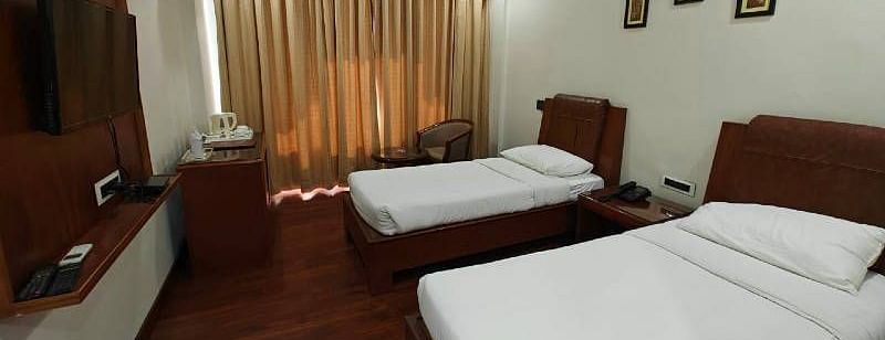 A spacious Luxury Room with two single beds along with beige coloured curtains covering the windows - Hotel Gold, Panipat