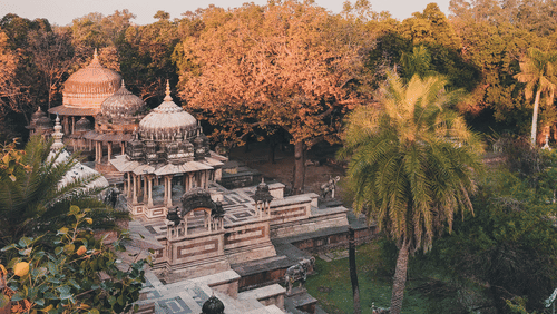 High-angle scenic view looking down onto a stone Kshar Bag temple building complex nestled within thick trees and palm plants.