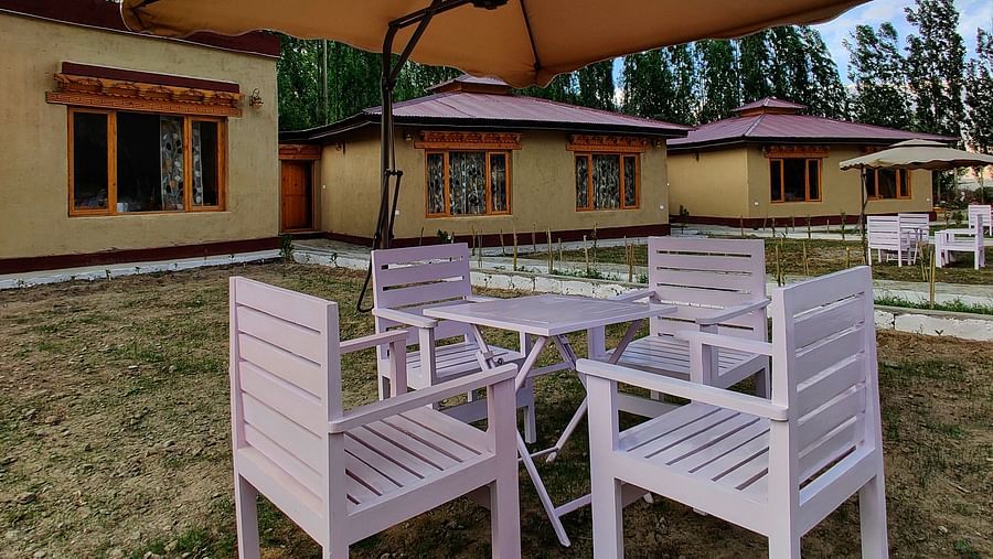 Outdoor seating and tables with umbrellas at the White Sands Resort, Ladakh providing a shaded space with a view of the surrounding landscape.