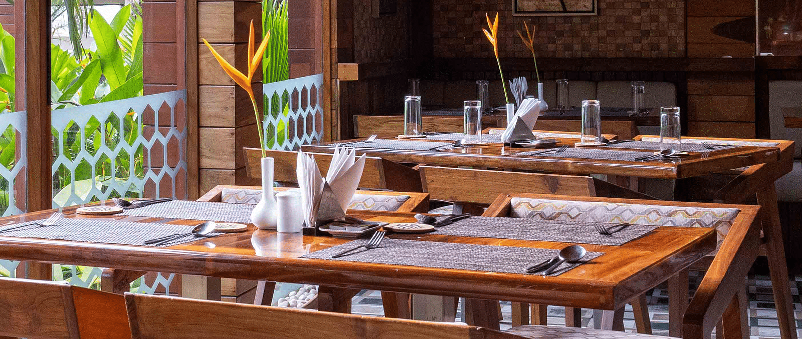 A restaurant with wooden furniture, with a balcony view to the lush greenery outside.