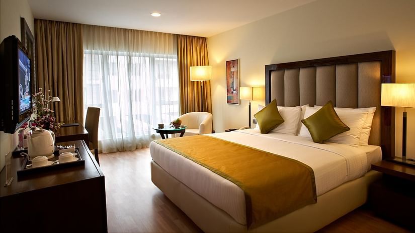 An image of a bedroom featuring double size bed, a flat TV screen, a cabinet, a sofa and centre table, and a few lamps at Adarsh Hamilton