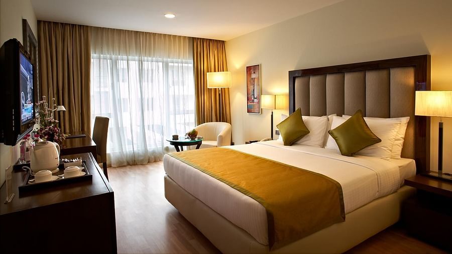An image of a bedroom featuring double size bed, a flat TV screen, a cabinet, a sofa and centre table, and a few lamps at Adarsh Hamilton