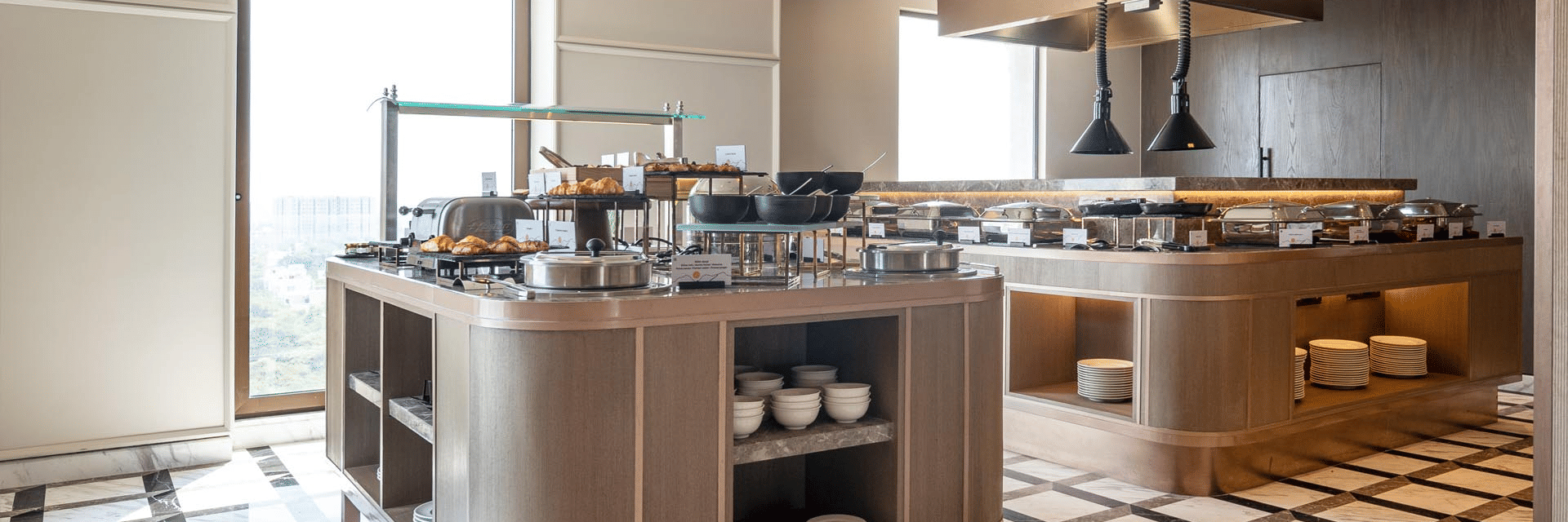 A modern buffet service station at The Residency Signature Madurai featuring wooden counters, warm lighting, and a checkered floor pattern.