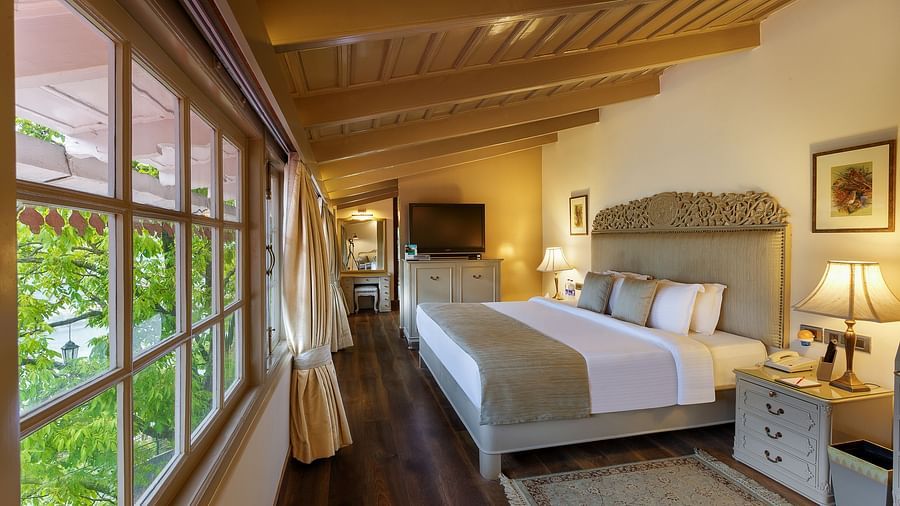 Side view of a room with TV, bed, lamp and glass windows - the naini retreat, nainital.
