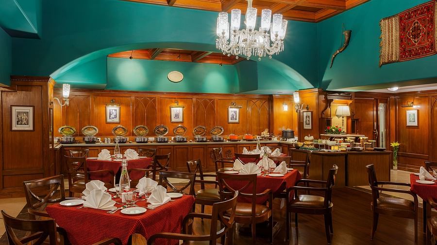 An image of Indoor view of the dining section at The Naini Retreat, Nainital, with sets of chairs and tables placed around the chandelier on the ceiling.