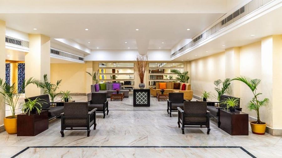 A seating lobby area with indoor plants, Chairs and Table  at Golden Tulip, Udaipur.