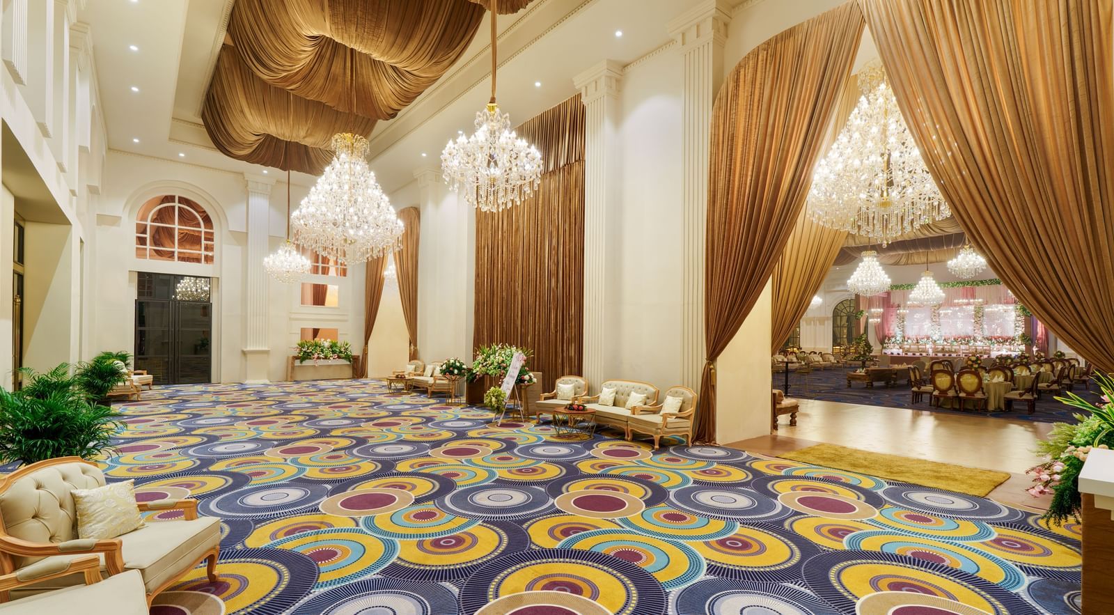  The opulent lobby of Nirvana Luxury Hotel, Ludhiana, showcasing a patterned carpet, comfortable seating areas, elegant chandeliers, and draped golden curtains.