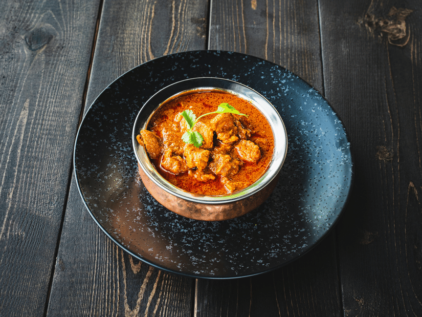 Bowl of Chettinad chicken curry served in a traditional vessel, rich gravy glistening, placed on a dark rustic wooden table