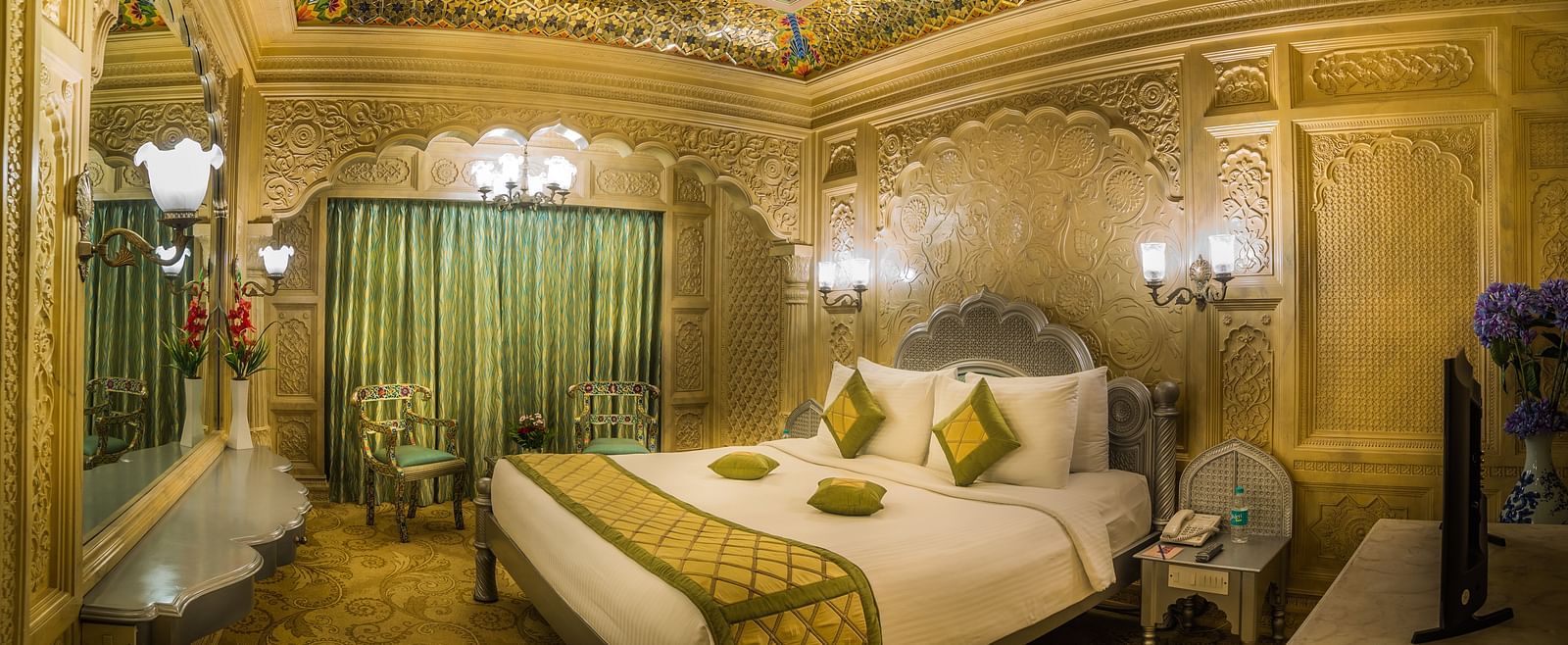A sumptuous hotel room that combines luxury with cultural artistry, featuring elaborate woodwork and plush furnishings A grand hotel suite with an opulent red and white decor, large bed, and seating area, reflecting a traditional style at Sitara Luxury Hot