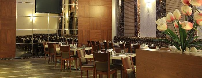 A grand dining area with high ceilings, wooden panel walls, and soft lighting for an upscale experience. - Dhanalakshmi Srinivasan Hotels, Perambalur