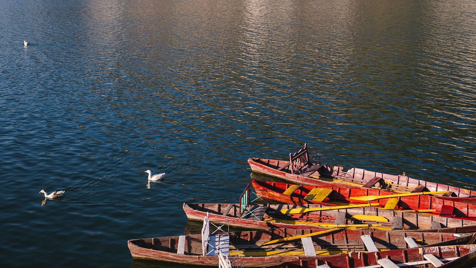 Boats are neatly arranged on a serene lake, surrounded by towering mountains.