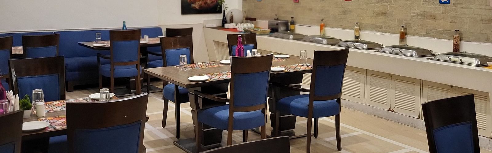An image of a restaurant featuring multiple sets of chairs and tables where plates, cutlery and napkins are placed at Inde Hotel Signature Tower Gurgaon