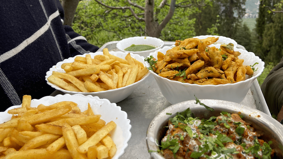 A close-up shot of a tray carrying 2 big servings of french fries, 1 serving of fritters, and 1 serving of an Indian dish garnished with coriander leaves at Amara Upepo - The Sky Village, Manali.