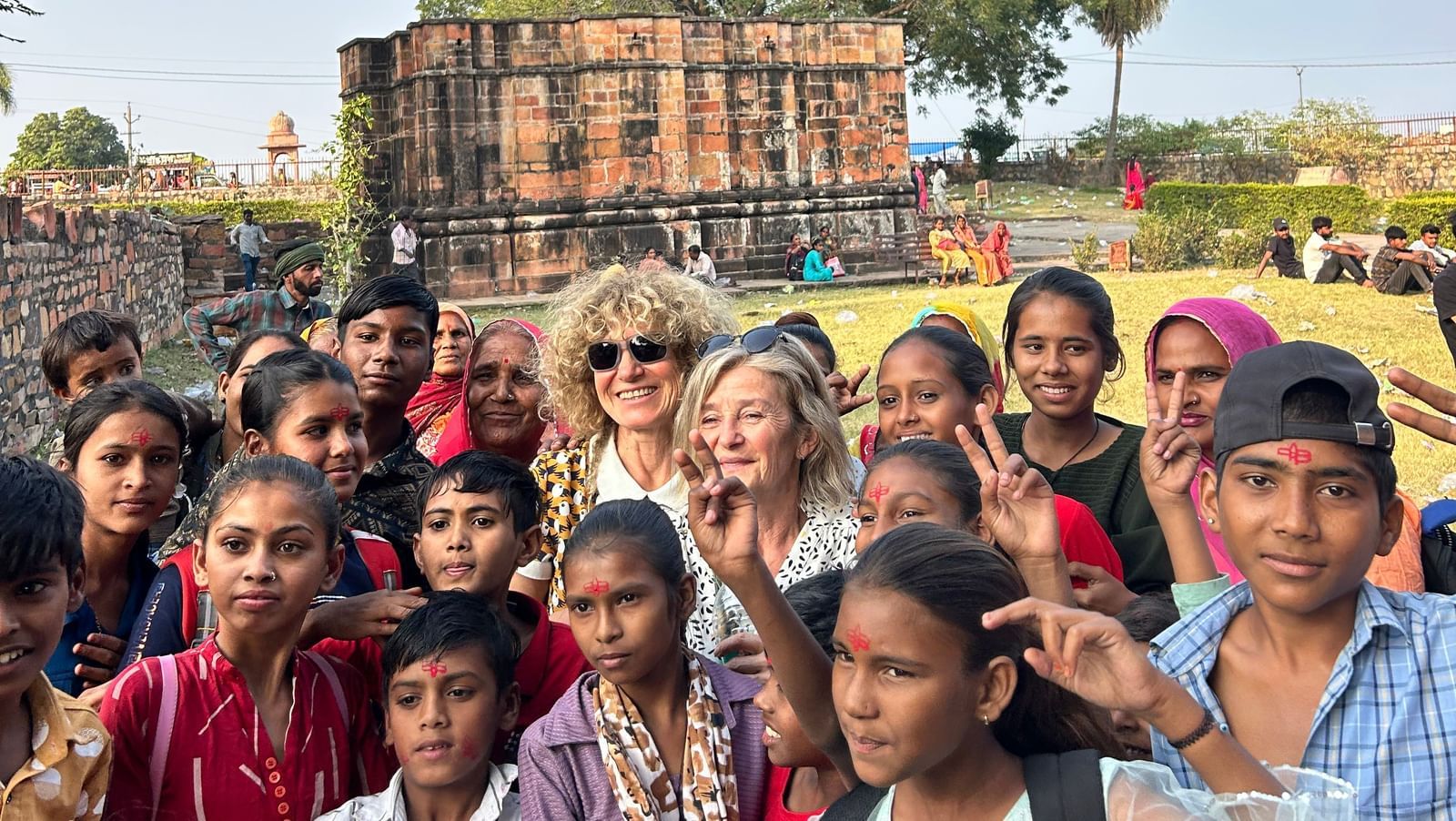 A group of young people, likely tourists, posing for a photo in front of an ancient stone ruin under a bright blue sky.