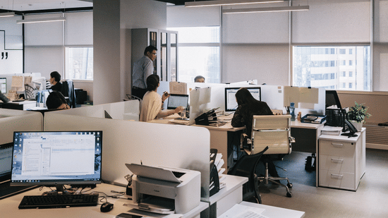 Open-plan office with workstations, desks, and overhead lighting.