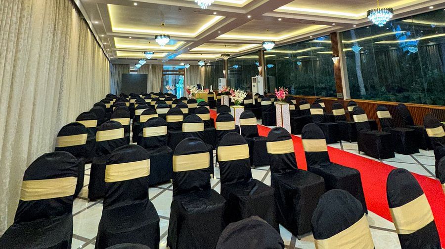 A hall with rows of black and gold chairs, a red carpet, and chandeliers at Silver Sand Sea Princess Beach Resort, Port Blair.