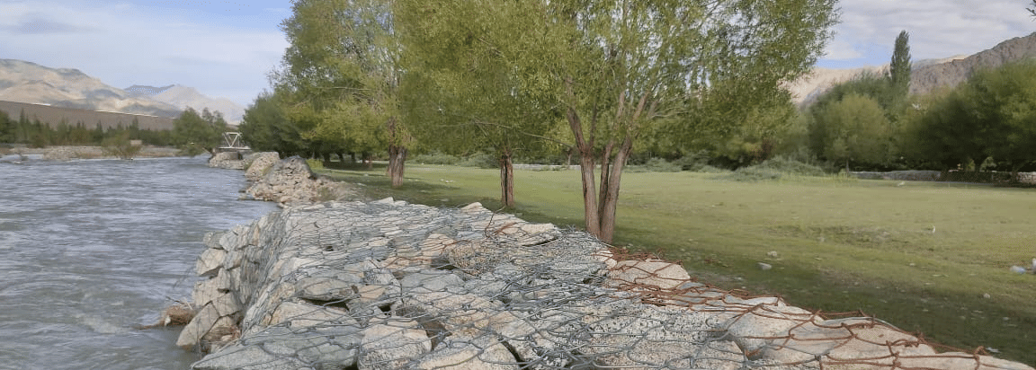 A sturdy stone-paved embankment running alongside a wide, fast-flowing river at Indus Serenity Retreat.