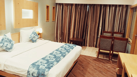 Premium Room at Hotel Mumbai House, Thane, featuring a king bed with teal patterned linen, wooden flooring, and window drapes.
