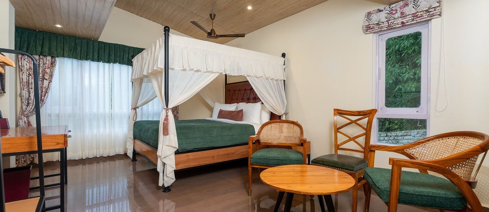 Premium Room featuring a large bed with curtains neatly tied to rods on all four sides, also includes chairs and tables arranged neatly.