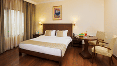 Superior Room Le Lac Sarovar Portico Ranchi featuring a bed, a work station, a chair, and a window with curtains drawn.
